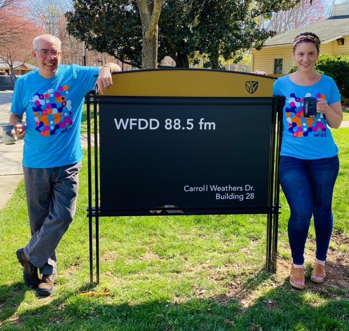 Two WFDD employees standing by the WFDD sign on Wake Forest University's Campus.