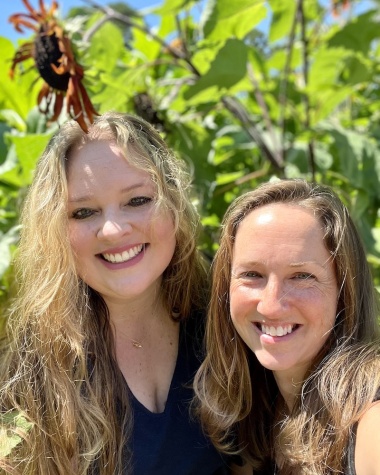 Sonsera and Julien, members of WFDD's Donor Services team, smile in front of sunflowers.