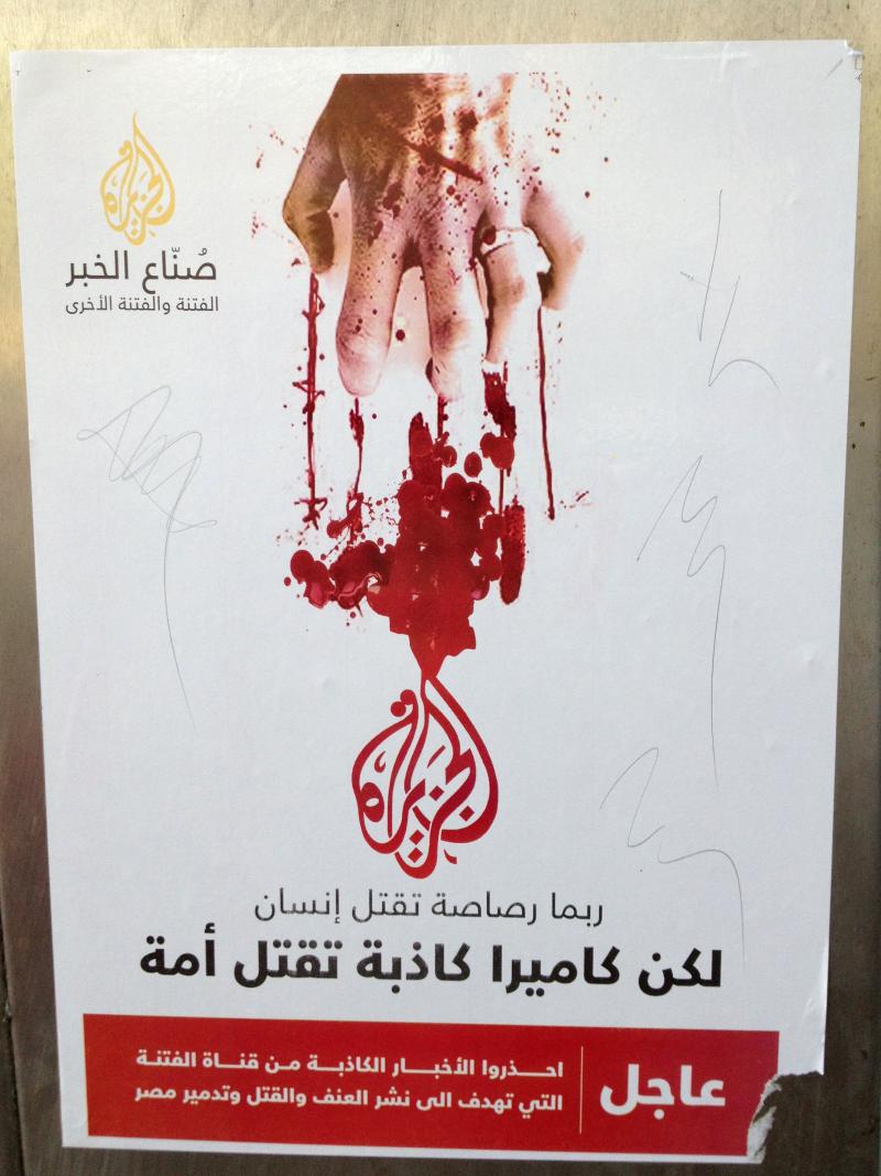 Posters in Cairo show Al-Jazeera's logo in red with a bloody hand scratching at it. A bullet can kill a man, the poster says, but a lying camera can kill a nation. Posters in Cairo show Al-Jazeera's logo in red with a bloody hand scratching at it. A bullet can kill a man, the poster says, but a lying camera can kill a nation.
