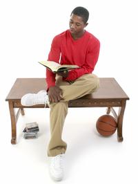 Casual man sitting on a table reading a book, with a stack of video games and a basketball nearby. Casual man sitting on a table reading a book, with a stack of video games and a basketball nearby.