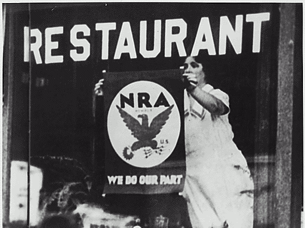 A woman hangs a National Industrial Recovery Act poster in the window of a restaurant. A woman hangs a National Industrial Recovery Act poster in the window of a restaurant.