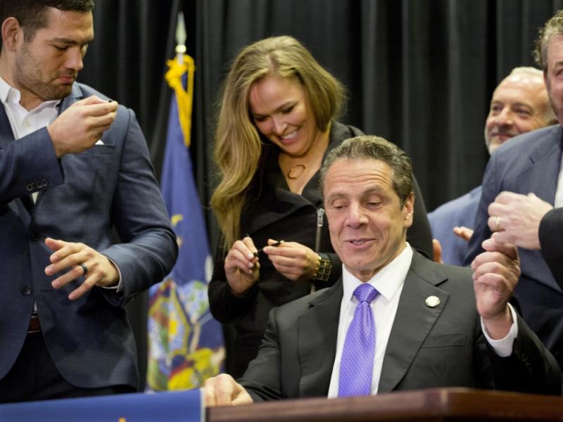 Gov. Andrew Cuomo (center) signed into law a measure that will allow professional mixed martial arts in New York. Behind him are UFC athletes Chris Weidman (left) and Ronda Rousey. Gov. Andrew Cuomo (center) signed into law a measure that will allow professional mixed martial arts in New York. Behind him are UFC athletes Chris Weidman (left) and Ronda Rousey.