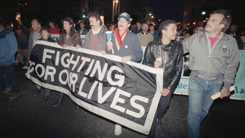 Marchers at a candlelight vigil in San Francisco, Calif., carry a banner to call attention to the continuing battle against AIDS on May 29, 1989. The city was home to the nation's first AIDS special care unit. The unit, which opened in 1983, is the subjec Marchers at a candlelight vigil in San Francisco, Calif., carry a banner to call attention to the continuing battle against AIDS on May 29, 1989. The city was home to the nation's first AIDS special care unit. The unit, which opened in 1983, is the subjec