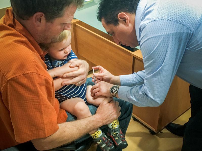 Erik Vance holds his son while a pediatrician administers vaccinations. Erik Vance holds his son while a pediatrician administers vaccinations.