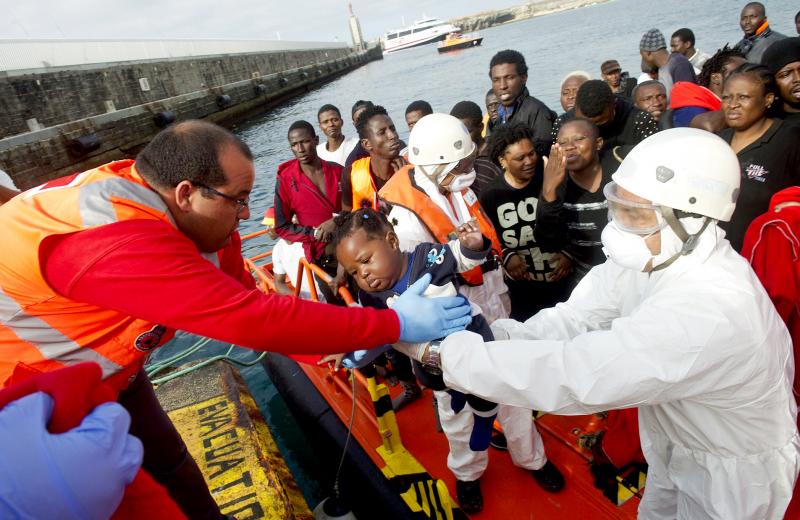 An African migrant infant is handed off by a member of the Red Cross to a member of the Spanish coast guard in the port of Tarifa on Tuesday. An African migrant infant is handed off by a member of the Red Cross to a member of the Spanish coast guard in the port of Tarifa on Tuesday.