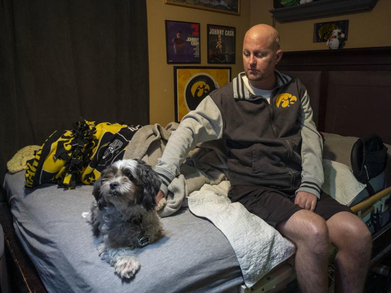 Jon Miller sits in his bedroom with his dog, Carlos, whom he received as a present for successfully completing cancer treatment a decade ago. Miller sustained severe brain damage, and requires the help of home health aides to continue living in his home. Jon Miller sits in his bedroom with his dog, Carlos, whom he received as a present for successfully completing cancer treatment a decade ago. Miller sustained severe brain damage, and requires the help of home health aides to continue living in his home.