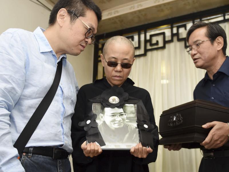 In a photo provided Saturday by the Shenyang Municipal Information Office, Liu Xia, center, the widow of Chinese dissident Liu Xiaobo, holds a portrait of him during his funeral. She stands with Liu Hui, her younger brother (left) and Liu Xiaoxuan, the yo In a photo provided Saturday by the Shenyang Municipal Information Office, Liu Xia, center, the widow of Chinese dissident Liu Xiaobo, holds a portrait of him during his funeral. She stands with Liu Hui, her younger brother (left) and Liu Xiaoxuan, the yo
