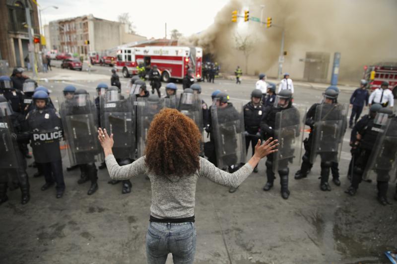 A woman faces a line of Baltimore police officers in riot gear. A woman faces a line of Baltimore police officers in riot gear.