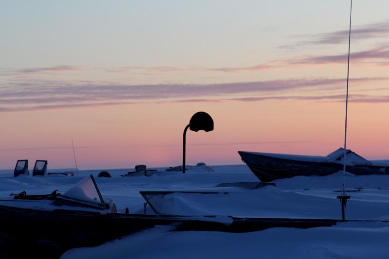 Basketball hoop near boats buried in the winter snow. Shishmaref is just a few dozen miles below the Arctic Circle, and in the depths of winter the sun rises close to noon. Basketball hoop near boats buried in the winter snow. Shishmaref is just a few dozen miles below the Arctic Circle, and in the depths of winter the sun rises close to noon.