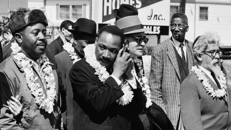 Martin Luther King, Jr. listening to a transistor radio in the front line of the third march from Selma to Montgomery, Alabama, to campaign for proper registration of black voters, March 23, 1965. Ralph Abernathy (second from left), Ralph Bunche (third fr Martin Luther King, Jr. listening to a transistor radio in the front line of the third march from Selma to Montgomery, Alabama, to campaign for proper registration of black voters, March 23, 1965. Ralph Abernathy (second from left), Ralph Bunche (third fr