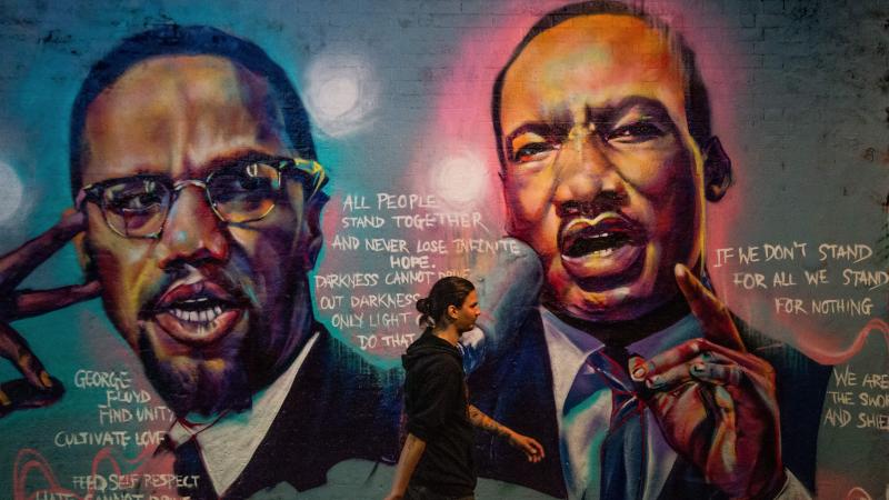 A man walks past a mural of Malcom X and Martin Luther King Jr. in London. A man walks past a mural of Malcom X and Martin Luther King Jr. in London.