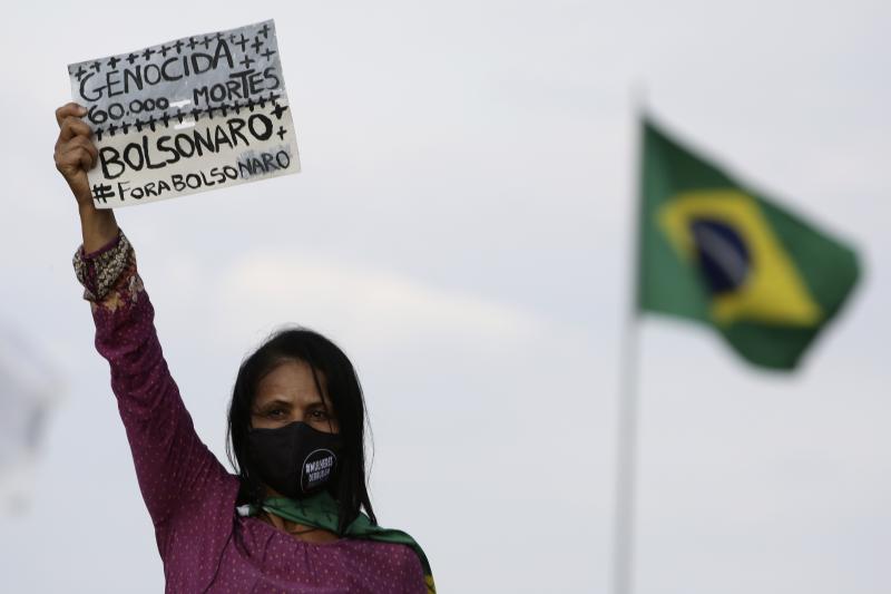 A women's movement activist holds a sign that reads in Portuguese "Genocide 60 thousand deaths, Bolsonaro out," during a protest against the government's handling of the pandemic earlier this month. A women's movement activist holds a sign that reads in Portuguese "Genocide 60 thousand deaths, Bolsonaro out," during a protest against the government's handling of the pandemic earlier this month.