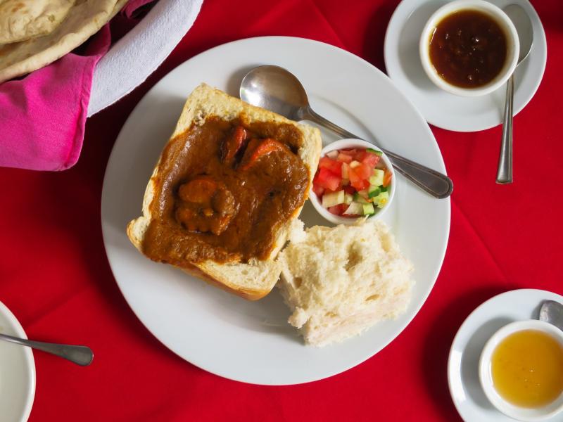 Indian Oven's bunny chow features shrimp with a side of tomatoes and cucumbers. The restaurant is located in Hout Bay, a suburb of Cape Town. Indian Oven's bunny chow features shrimp with a side of tomatoes and cucumbers. The restaurant is located in Hout Bay, a suburb of Cape Town.