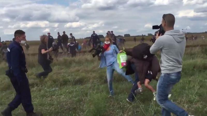 A videographer for a Hungarian TV network trips a migrant holding a young boy who was running away from police. The camerawoman was fired. A videographer for a Hungarian TV network trips a migrant holding a young boy who was running away from police. The camerawoman was fired.