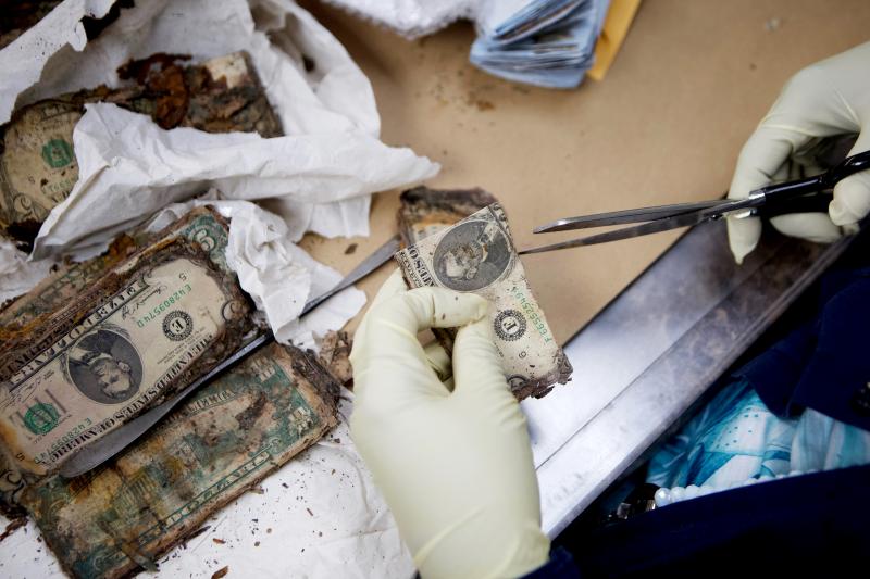 An employee of the Mutilated Currency Division cuts a damaged dollar to "duplicate" it and identify other bills with the cut fragment. An employee of the Mutilated Currency Division cuts a damaged dollar to "duplicate" it and identify other bills with the cut fragment.