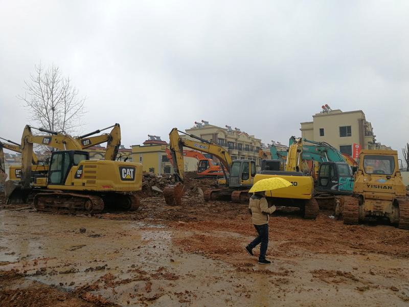 A man holding an umbrella walks past excavators at the construction site where a new quarantine and treatment center is being built to treat patients of a new coronavirus. A man holding an umbrella walks past excavators at the construction site where a new quarantine and treatment center is being built to treat patients of a new coronavirus.