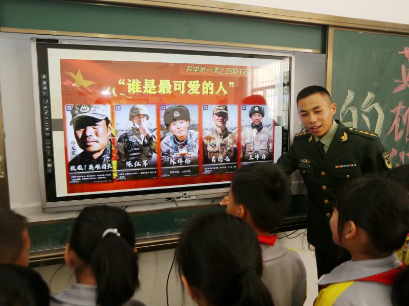 A paramilitary police officer talks next to a screen showing frontier soldiers of the People's Liberation Army during an event at a primary school in Wuzhishan, Hainan province, China, on Feb. 22. On the screen are (L-R) Qi Fabao, who was seriously wounde A paramilitary police officer talks next to a screen showing frontier soldiers of the People's Liberation Army during an event at a primary school in Wuzhishan, Hainan province, China, on Feb. 22. On the screen are (L-R) Qi Fabao, who was seriously wounde