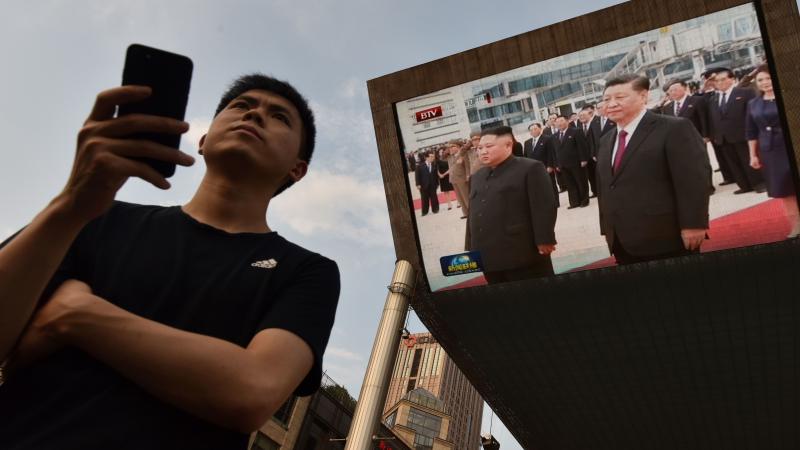 A man waits for a taxi in Beijing as news footage of Chinese President Xi Jinping (right) being greeted in Pyongyang by North Korean leader Kim Jong Un is shown on a large screen outside a shopping mall. A man waits for a taxi in Beijing as news footage of Chinese President Xi Jinping (right) being greeted in Pyongyang by North Korean leader Kim Jong Un is shown on a large screen outside a shopping mall.