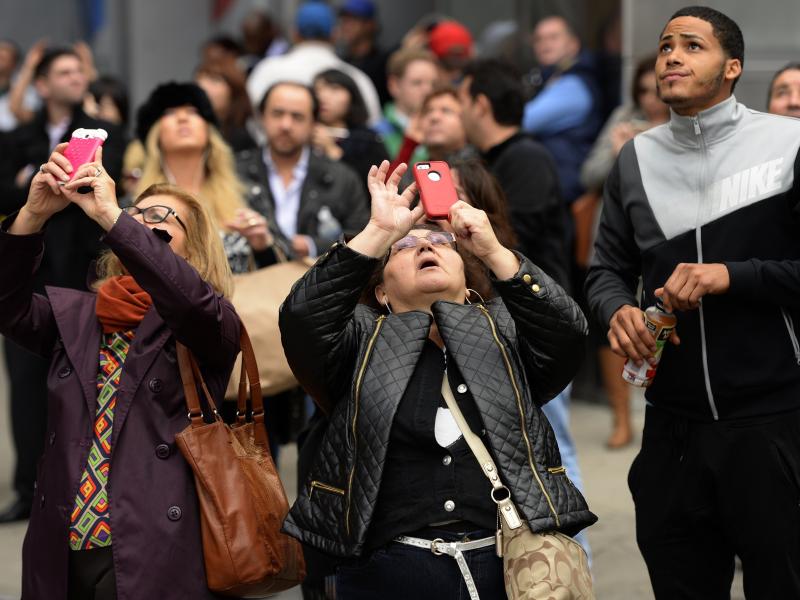 Onlookers take cell phone pictures of stranded window washers hanging from scaffolding on the side of One World Trade Center. Onlookers take cell phone pictures of stranded window washers hanging from scaffolding on the side of One World Trade Center.
