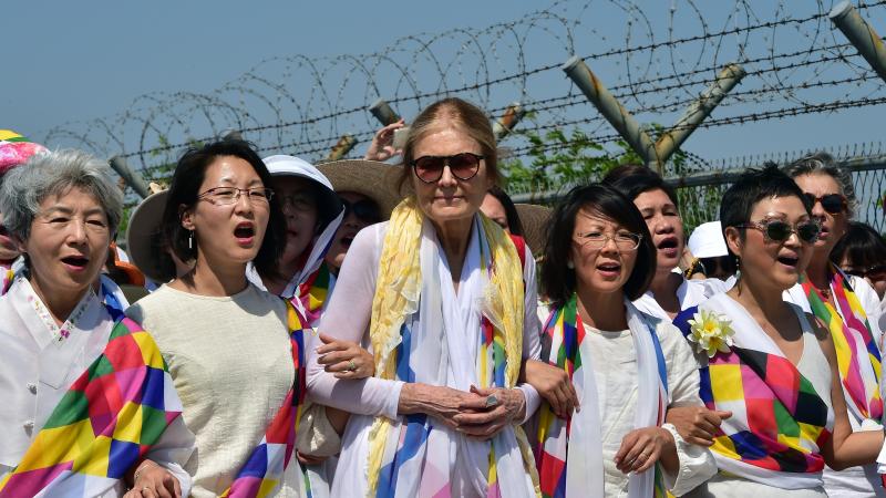 Gloria Steinem and South Korean peace activists march along a military fence at a checkpoint after crossing the border separating North and South Korea. Gloria Steinem and South Korean peace activists march along a military fence at a checkpoint after crossing the border separating North and South Korea.