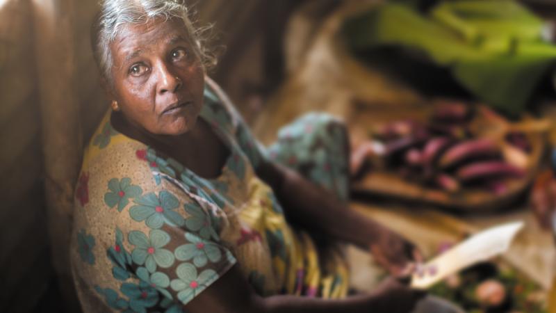 After losing her daughter during the war, Vijaya cares for her granddaughter Anjali. Despite not being able to afford fresh vegetables, she cooks nourishing sothis or stews made of coconut milk. After losing her daughter during the war, Vijaya cares for her granddaughter Anjali. Despite not being able to afford fresh vegetables, she cooks nourishing sothis or stews made of coconut milk.