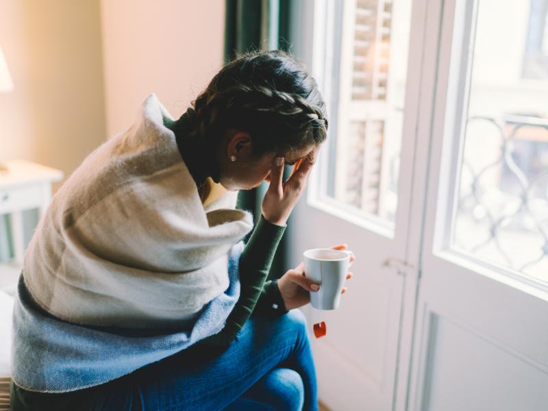 A woman with a temperature stays home, wrapped in a scarf while drinking hot tea. A woman with a temperature stays home, wrapped in a scarf while drinking hot tea.