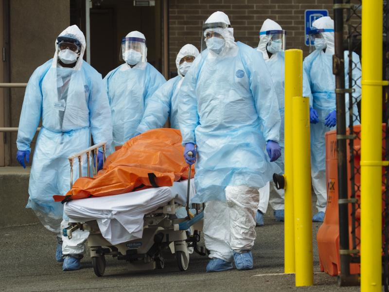 Medical workers in protective clothing move a body to a refrigerated overflow morgue outside the Wyckoff Heights Medical Center in Brooklyn on Thursday. Medical workers in protective clothing move a body to a refrigerated overflow morgue outside the Wyckoff Heights Medical Center in Brooklyn on Thursday.