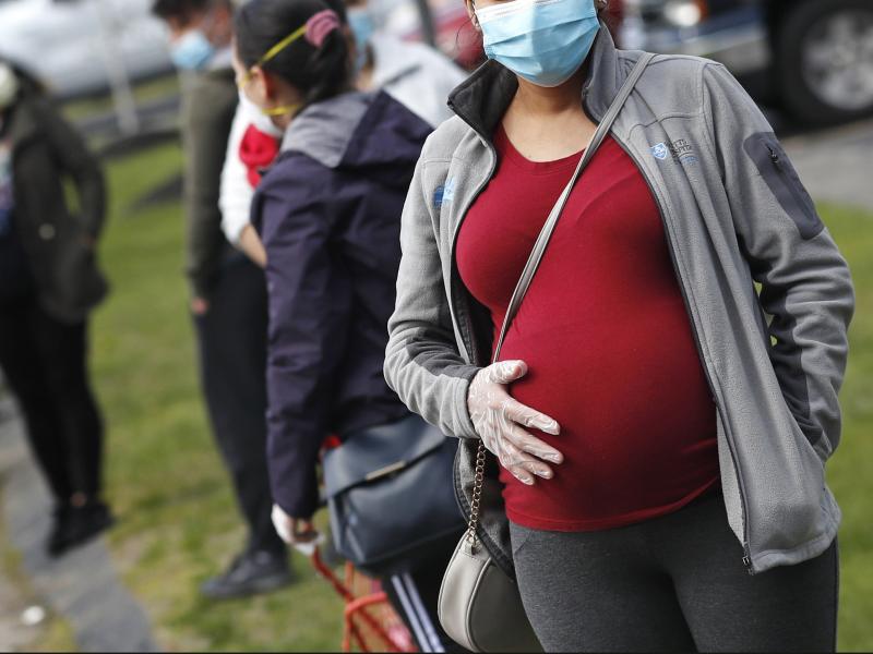 A pregnant woman waits in line for groceries at a food pantry in Waltham, Mass., during the coronavirus pandemic. A pregnant woman waits in line for groceries at a food pantry in Waltham, Mass., during the coronavirus pandemic.