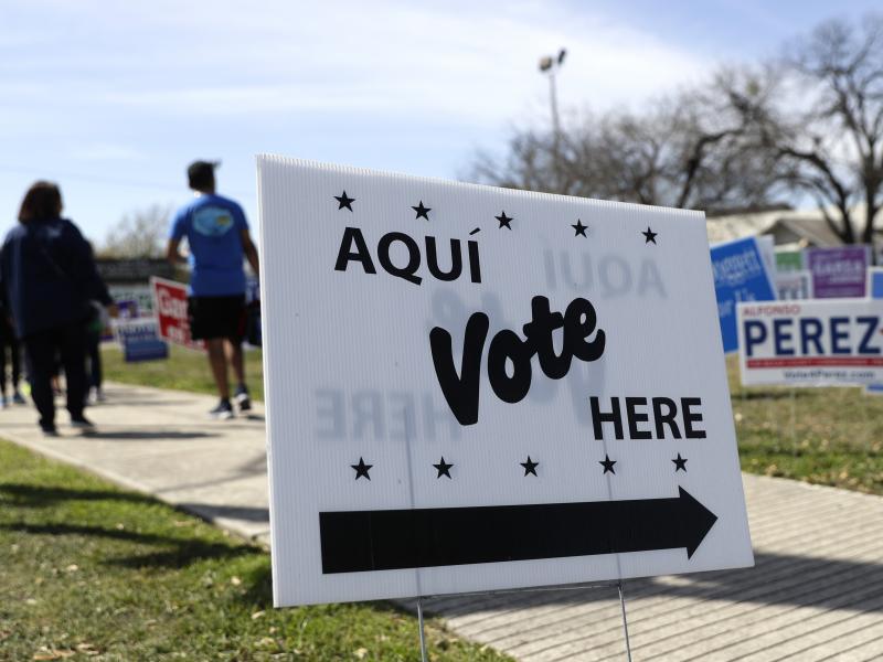 Pedestrians pass signs near a polling site in San Antonio in February. Pedestrians pass signs near a polling site in San Antonio in February.
