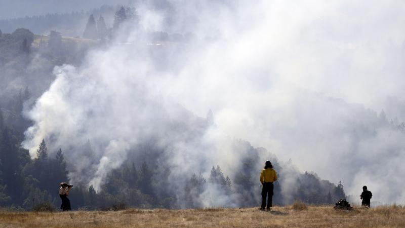 A firefighter (center) and two onlookers watch a smoldering wildfire from a hilltop in Oakville, Calif., on Sunday. A firefighter (center) and two onlookers watch a smoldering wildfire from a hilltop in Oakville, Calif., on Sunday.