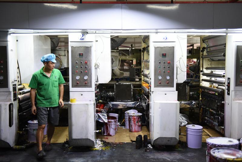 Workers in green polo shirts and blue caps monitor machines making plastic products at the Dongguan Fangjie Printing and Packaging Company. Workers in green polo shirts and blue caps monitor machines making plastic products at the Dongguan Fangjie Printing and Packaging Company.