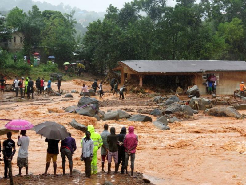Bystanders look on as floodwaters rage past a damaged building on the outskirts of Freetown on Monday, after mudslides struck near the capital of the west African state of Sierra Leone. Bystanders look on as floodwaters rage past a damaged building on the outskirts of Freetown on Monday, after mudslides struck near the capital of the west African state of Sierra Leone.