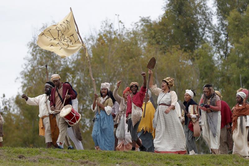 People march along the Mississippi River levee in Louisiana on Friday as they perform in a reenactment of the 1811 German Coast Uprising. People march along the Mississippi River levee in Louisiana on Friday as they perform in a reenactment of the 1811 German Coast Uprising.