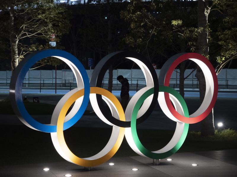 A man is seen through the Olympic rings in front of the New National Stadium in Tokyo, on Tuesday. The Summer Games have been delayed amid the coronavirus pandemic. A man is seen through the Olympic rings in front of the New National Stadium in Tokyo, on Tuesday. The Summer Games have been delayed amid the coronavirus pandemic.