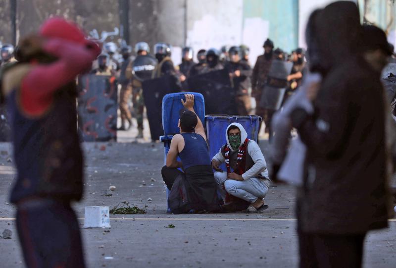 Iraqi demonstrators take cover from security forces behind trash cans during clashes in the city of Karbala on Thursday. Iraqi demonstrators take cover from security forces behind trash cans during clashes in the city of Karbala on Thursday.