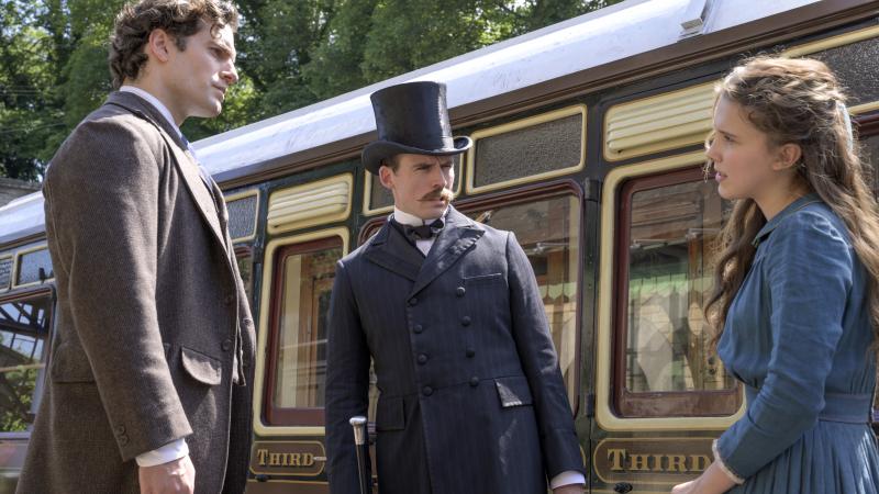 "The train's afoot!": (L to R) Sherlock (Henry Cavill) and Mycroft (Sam Claflin) literally look down on their younger sister Enola (Millie Bobby Brown) in Netflix's Enola Holmes. "The train's afoot!": (L to R) Sherlock (Henry Cavill) and Mycroft (Sam Claflin) literally look down on their younger sister Enola (Millie Bobby Brown) in Netflix's Enola Holmes.