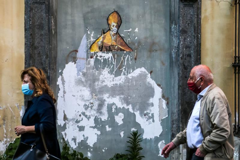 Pedestrians in face masks pass a mural in Naples depicting the city's patron saint, St. Gennaro, in a face mask too. Italy has set a timeline for lifting its strict coronavirus travel restrictions, after its outbreak overwhelmed medical centers across the Pedestrians in face masks pass a mural in Naples depicting the city's patron saint, St. Gennaro, in a face mask too. Italy has set a timeline for lifting its strict coronavirus travel restrictions, after its outbreak overwhelmed medical centers across the