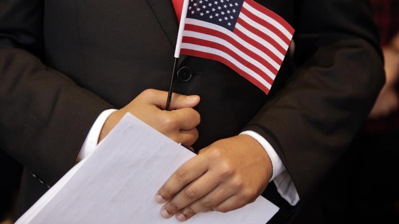 A newly sworn-in U.S. citizen holds a U.S. flag and documents during a naturalization ceremony in 2018 at the John F. Kennedy Presidential Library and Museum in Boston. A newly sworn-in U.S. citizen holds a U.S. flag and documents during a naturalization ceremony in 2018 at the John F. Kennedy Presidential Library and Museum in Boston.