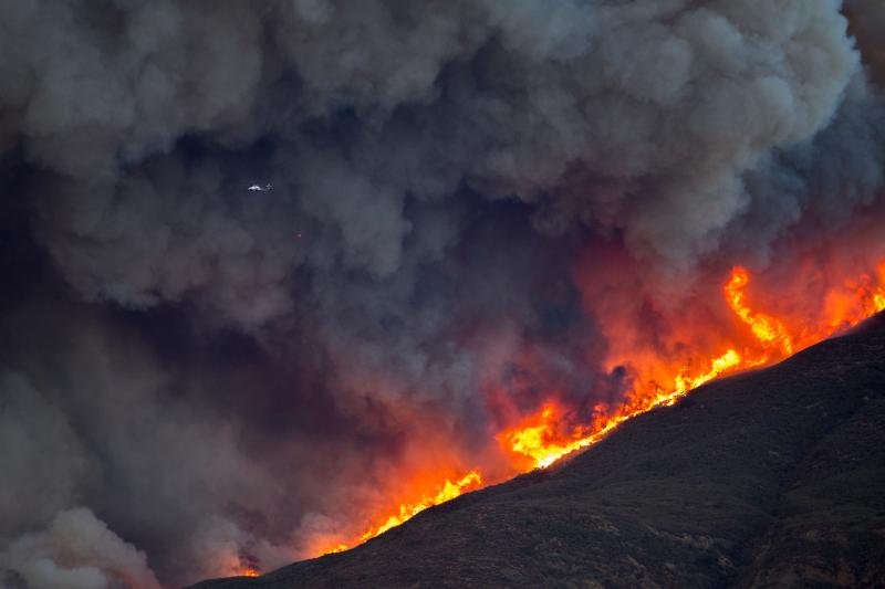 A firefighting helicopter is dwarfed by smoke and flames during Thomas Fire on Thursday. A firefighting helicopter is dwarfed by smoke and flames during Thomas Fire on Thursday.