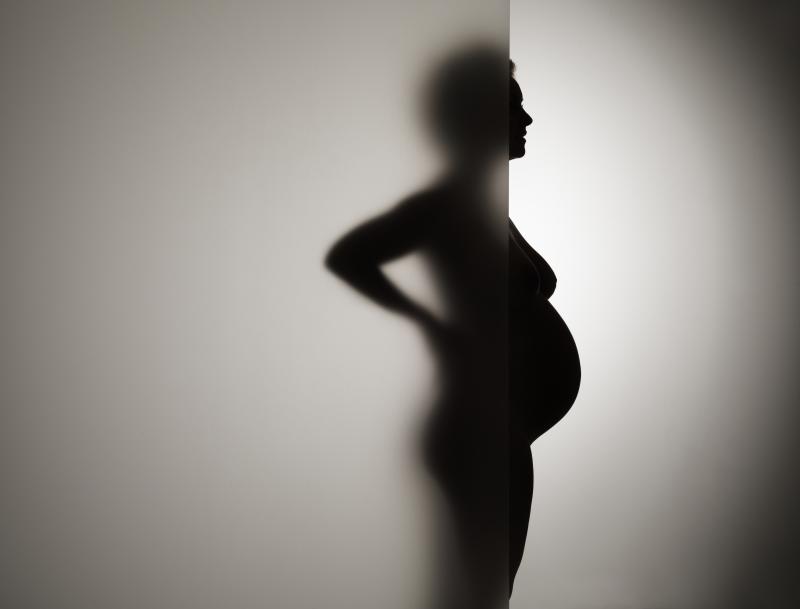 A pregnant woman stands behind frosty glass. A pregnant woman stands behind frosty glass.