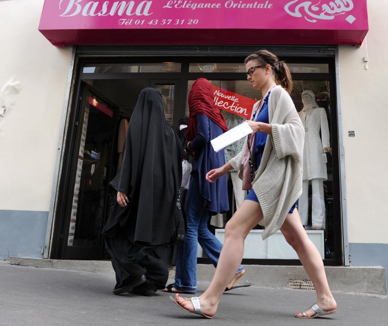 Three women, two of them partially veiled, walk past a hijabs shop in Paris. The wearing of the veil has been a serious point of contention in France, with the government banning its use in public schools and the wearing of face-covering garments, includi Three women, two of them partially veiled, walk past a hijabs shop in Paris. The wearing of the veil has been a serious point of contention in France, with the government banning its use in public schools and the wearing of face-covering garments, includi