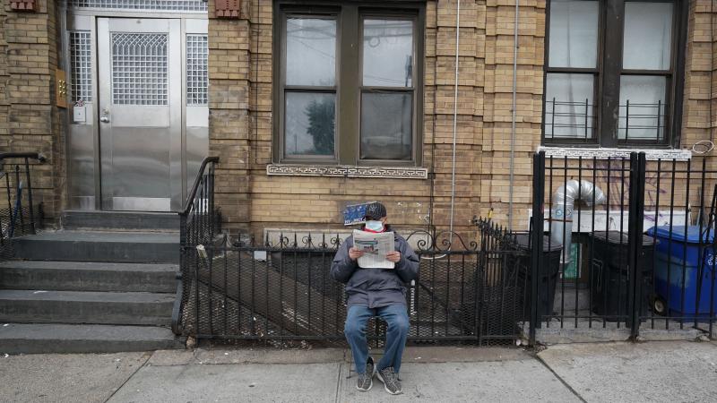 A man wearing a surgical mask reads the newspaper on the sidewalk late last month in New York City. The city's leaders said Thursday that social distancing is still necessary. A man wearing a surgical mask reads the newspaper on the sidewalk late last month in New York City. The city's leaders said Thursday that social distancing is still necessary.