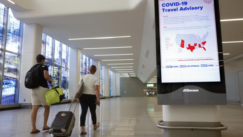 Arriving travelers walk by a COVID-19 travel advisory sign in the baggage claim area at New York City's LaGuardia Airport. New York state is requiring travelers from states on its quarantine list to show proof that they've completed a form with their cont Arriving travelers walk by a COVID-19 travel advisory sign in the baggage claim area at New York City's LaGuardia Airport. New York state is requiring travelers from states on its quarantine list to show proof that they've completed a form with their cont