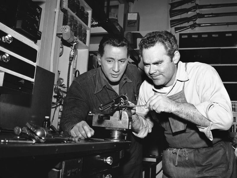 In this photo from a Hollywood studio gun department in 1958, Rodd Redwing (left) checks the final adjustment that Bob Lane is making on a six-gun. Redwing is an actor and a teacher of western gun handling. Lane is one of the men who repair and service th In this photo from a Hollywood studio gun department in 1958, Rodd Redwing (left) checks the final adjustment that Bob Lane is making on a six-gun. Redwing is an actor and a teacher of western gun handling. Lane is one of the men who repair and service th
