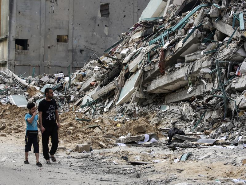Palestinian people walk past a destroyed tower. (Photo by Ahmed Zakot/SOPA Images/LightRocket via Getty Images) Palestinian people walk past a destroyed tower. (Photo by Ahmed Zakot/SOPA Images/LightRocket via Getty Images)