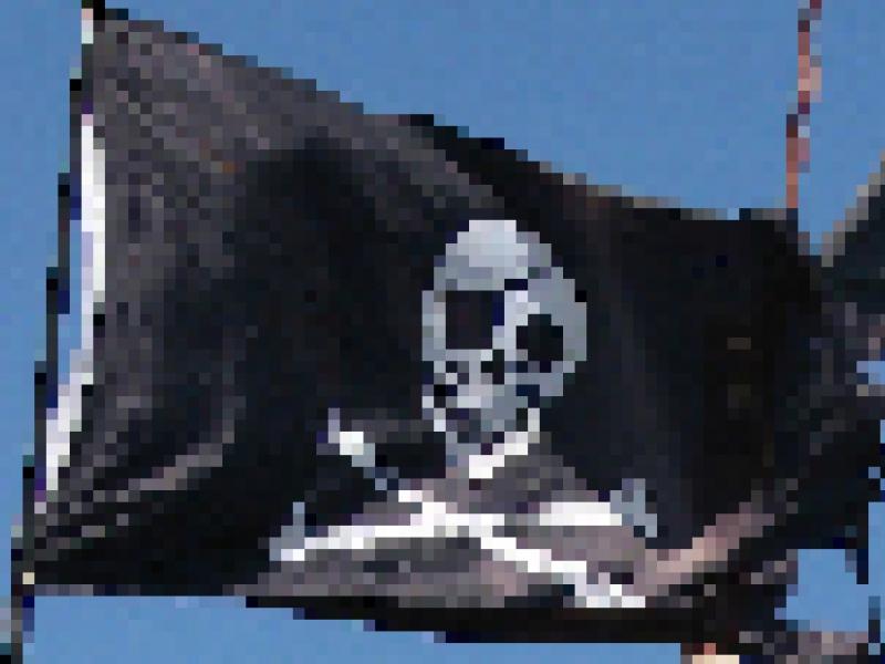 A classic pirate flag with white skull and crossbones on a black background. It's torn on the edges and flying against a bright blue sky. A classic pirate flag with white skull and crossbones on a black background. It's torn on the edges and flying against a bright blue sky.