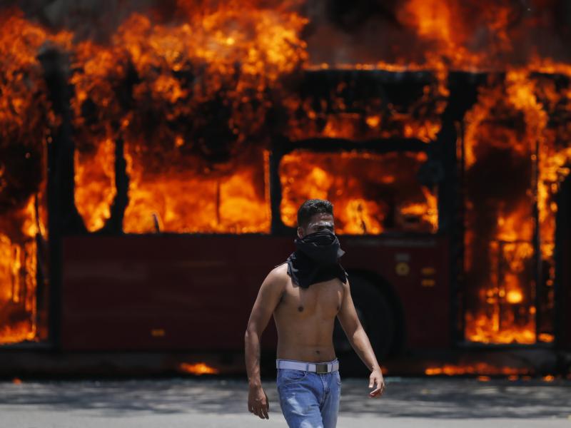 An anti-government protester walks near a bus that was set on fire by other protesters during clashes between rebel and loyalist soldiers in Caracas, Venezuela, on Tuesday. An anti-government protester walks near a bus that was set on fire by other protesters during clashes between rebel and loyalist soldiers in Caracas, Venezuela, on Tuesday.