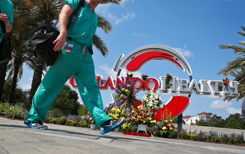Medical professionals walk by a makeshift memorial set up at the Orlando Health sign in June in Orlando, Fla. Medical professionals walk by a makeshift memorial set up at the Orlando Health sign in June in Orlando, Fla.