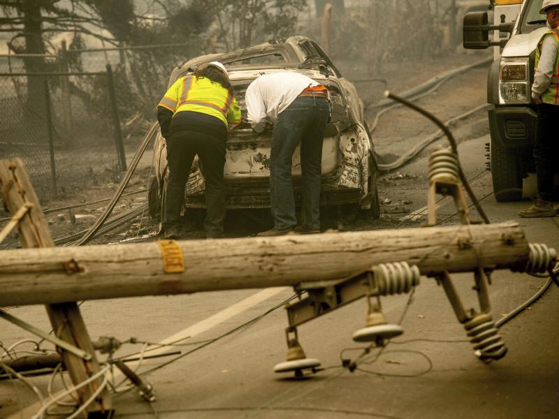 With a downed power utility pole in the foreground, residents of Paradise, Calif., examine a burned-out vehicle destroyed by last year's wildfire. With a downed power utility pole in the foreground, residents of Paradise, Calif., examine a burned-out vehicle destroyed by last year's wildfire.