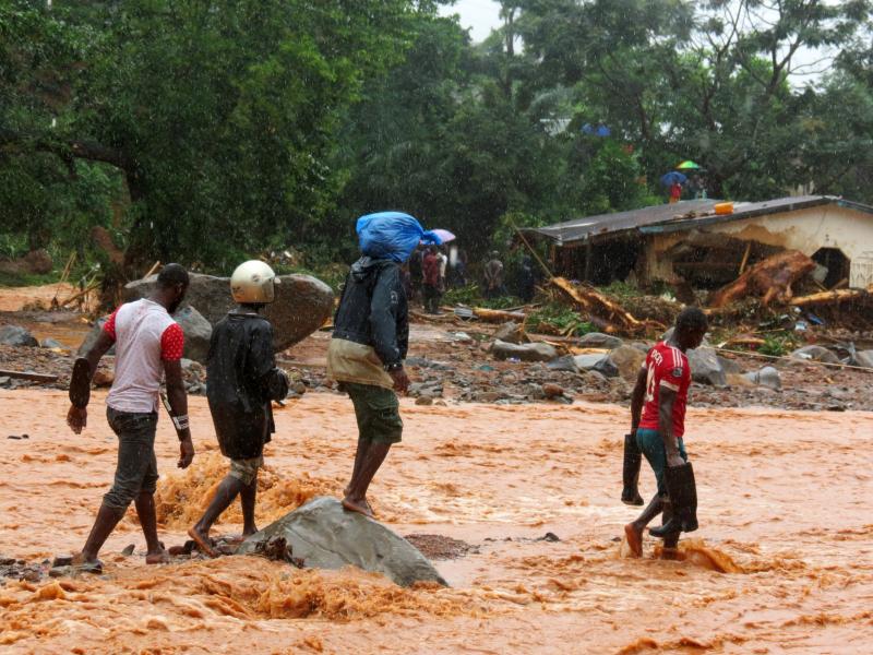 Residents pass a damaged building as they walk through floodwaters on the outskirts of Sierra Leone's capital, Freetown, on Monday. Residents pass a damaged building as they walk through floodwaters on the outskirts of Sierra Leone's capital, Freetown, on Monday.